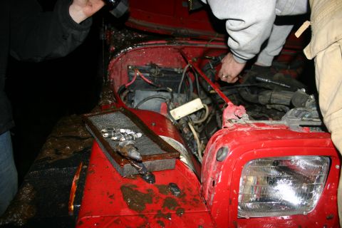 2003 Jeep TJ - Mud-covered Jeep TJ engine bay with people attempting repairs.