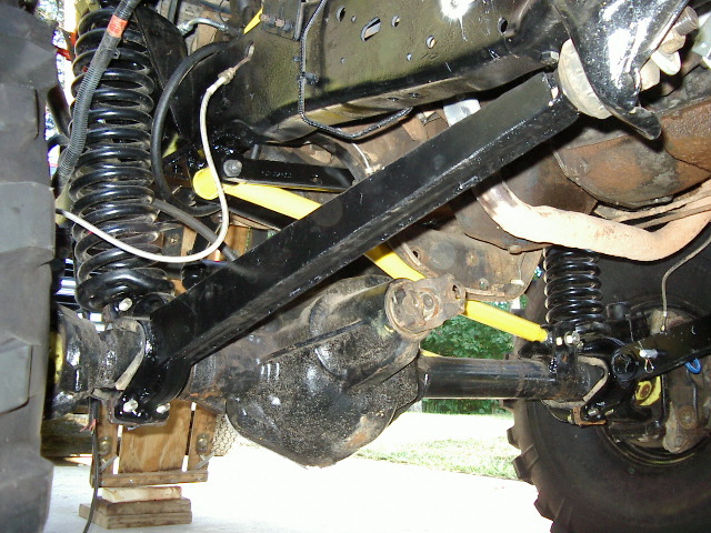 Close-up of a vehicle's front axle, differential, springs, and control arms. Some yellow shocks are visible