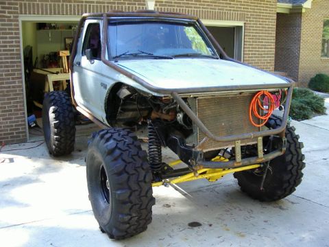 1985 Ford Bronco - Modified 1985 Ford Bronco with custom roll cage and large off-road tires sits in a driveway.