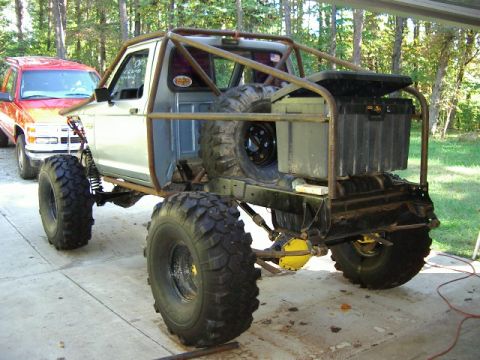 1985 Ford Bronco - A heavily modified pickup truck with an external roll cage and oversized tires is parked outdoors.