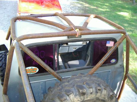 1985 Ford Bronco - Custom roll cage covers the rear of a truck, obscuring the interior and a spare tire mounted at the back.