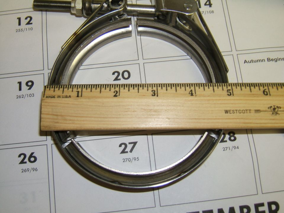 Metal exhaust clamp with a wooden ruler measuring its diameter over a calendar page