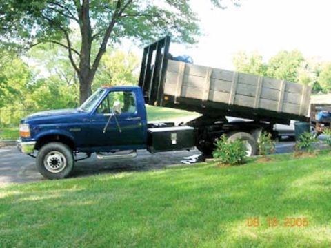 1991 Ford Bronco - Blue Ford F-Series dump truck parked on a grassy area with trees in the background.