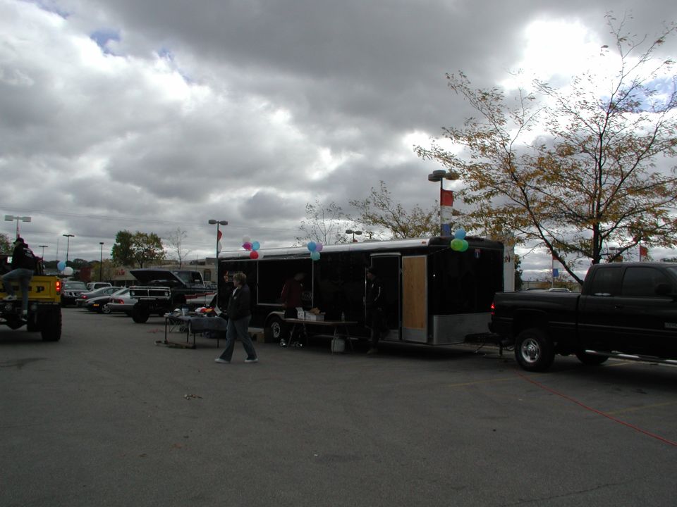 Black pickup truck parked next to a black trailer with balloons. Other vehicles and people are visible in the background