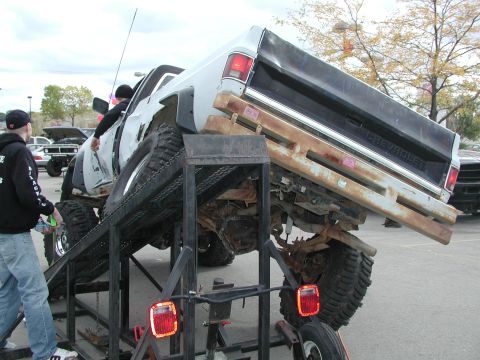 1977 Ford F-150 - White Chevrolet pickup truck is being loaded onto a ramp, showing its rear end and large tires.