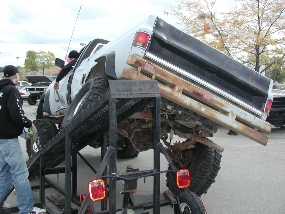 White Chevrolet pickup truck on a ramp, rear view, rusty bumper, large tires