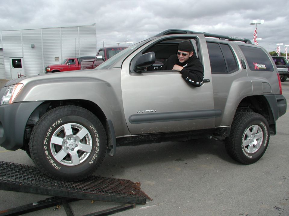 Guy in a silver Nissan Xterra with off-road tires, parked on a ramp. Red truck in background