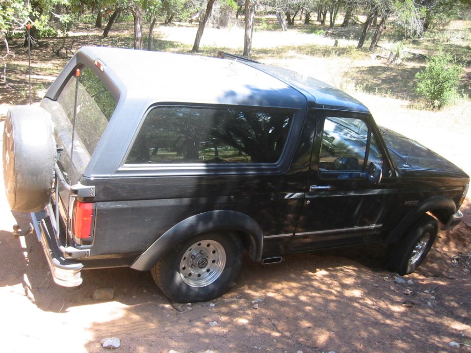 Black two-door Ford Bronco with gray hardtop and spare tire carrier, rear-left view