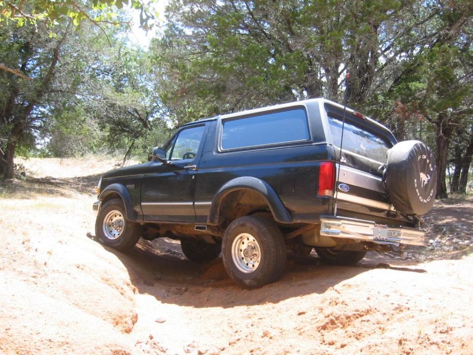 Black Ford Bronco with spare tire on tailgate climbing a sandy off-road rut