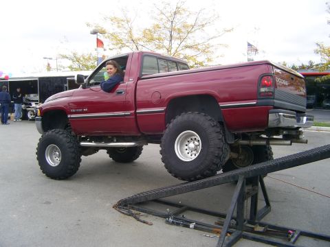 1977 Ford F-150 - Red Dodge Ram pickup truck with large tires is positioned on a ramp.