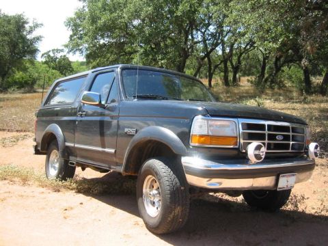 1995 Ford Bronco - This Ford Bronco is parked outdoors on a dirt road with trees in the background.