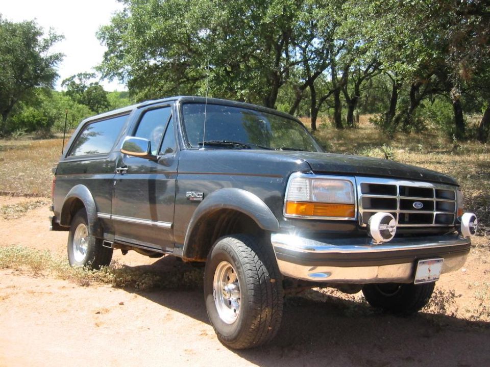 Dark gray Ford Bronco parked on dirt road, trees in background