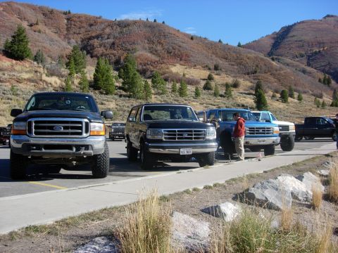 1987 Ford Bronco - Several trucks and SUVs are parked in a lot with a mountainous backdrop.