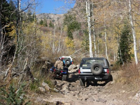 1987 Ford Bronco - Two SUVs navigate a challenging rocky trail in a wooded mountain area during the fall season.