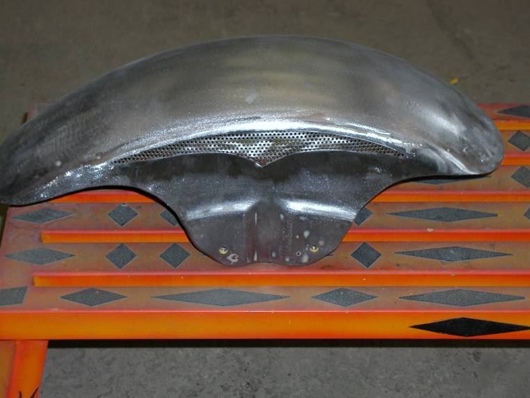 Bare metal motorcycle front fender with mesh vent on orange workbench
