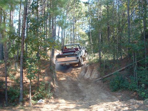 1993 Ford Bronco - A vehicle navigates a challenging off-road trail surrounded by dense trees.