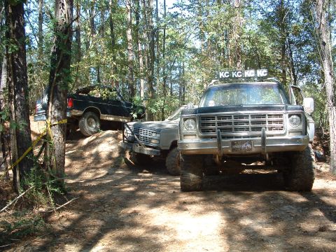 1993 Ford Bronco - Several off-road vehicles are parked on a dirt trail surrounded by trees.