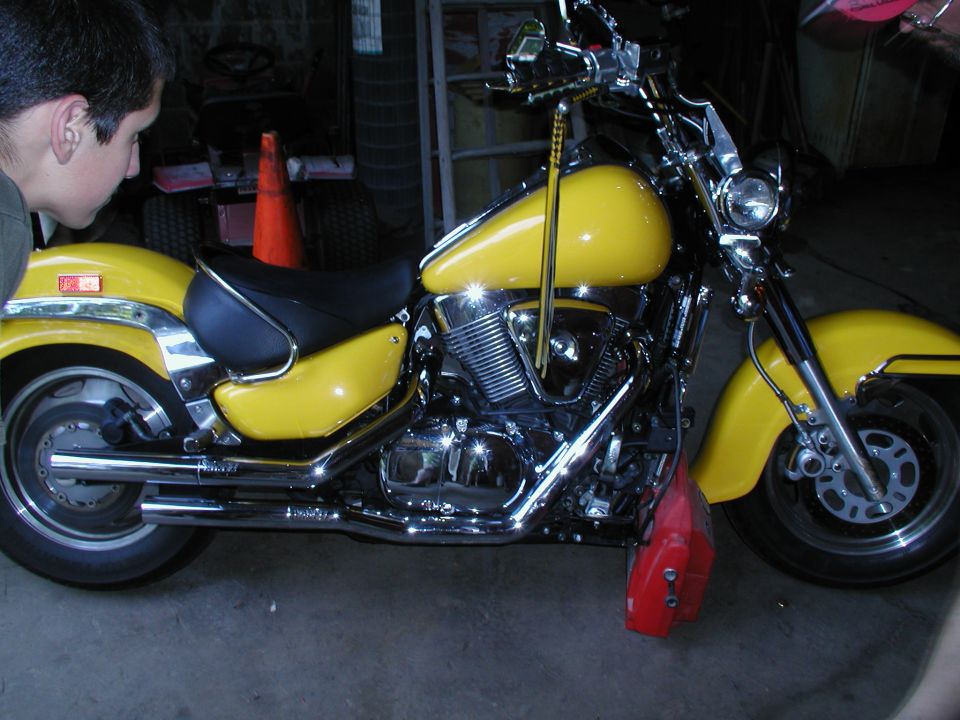 Yellow chrome cruiser motorcycle, left side view in garage with person at edge