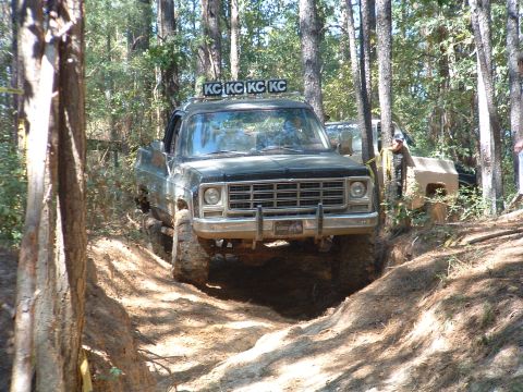 1993 Ford Bronco - This off-road truck, equipped with KC lights, navigates a challenging dirt trail through a wooded area, with another vehicle visible in the…