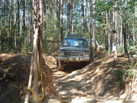 1993 Ford Bronco - An off-road vehicle navigates a wooded trail with caution tape visible on a tree.