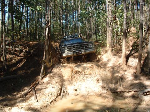1993 Ford Bronco - A truck navigates a muddy trail through a dense forest, kicking up water and dirt.