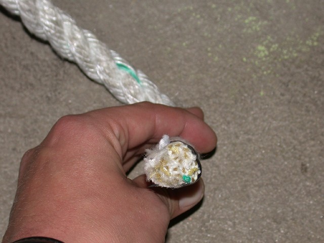 Hand holding frayed end of a thick white rope with green fibers visible inside