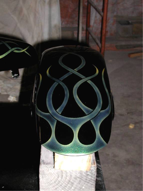 Black motorcycle fender with green and yellow ghost flames drying on a workbench