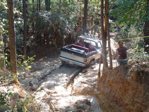 1993 Ford Bronco - An off-road vehicle navigates a muddy trail in a wooded area.