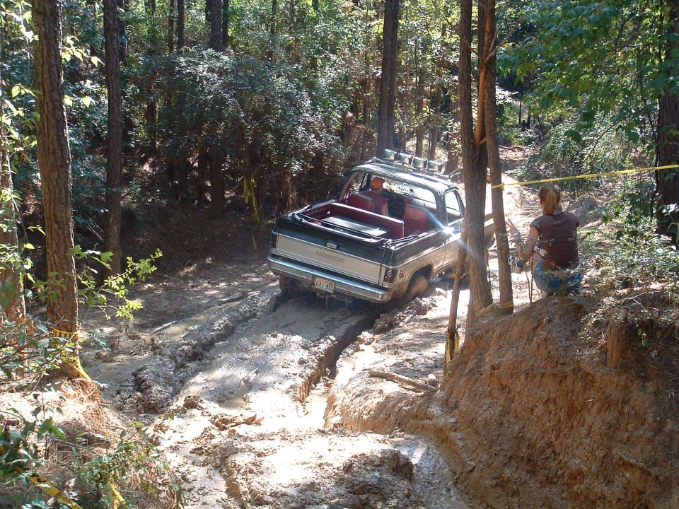 Black and silver off-road SUV with red interior driving through mud, rear view