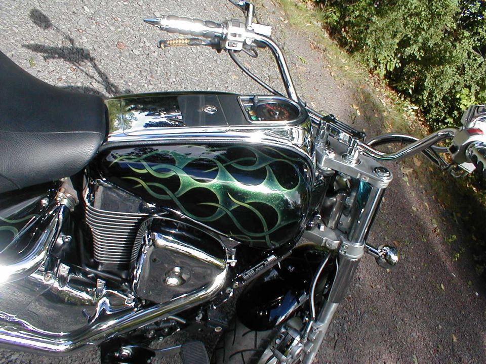 Cruiser motorcycle tank with green tribal flames and chrome bars, viewed from seat