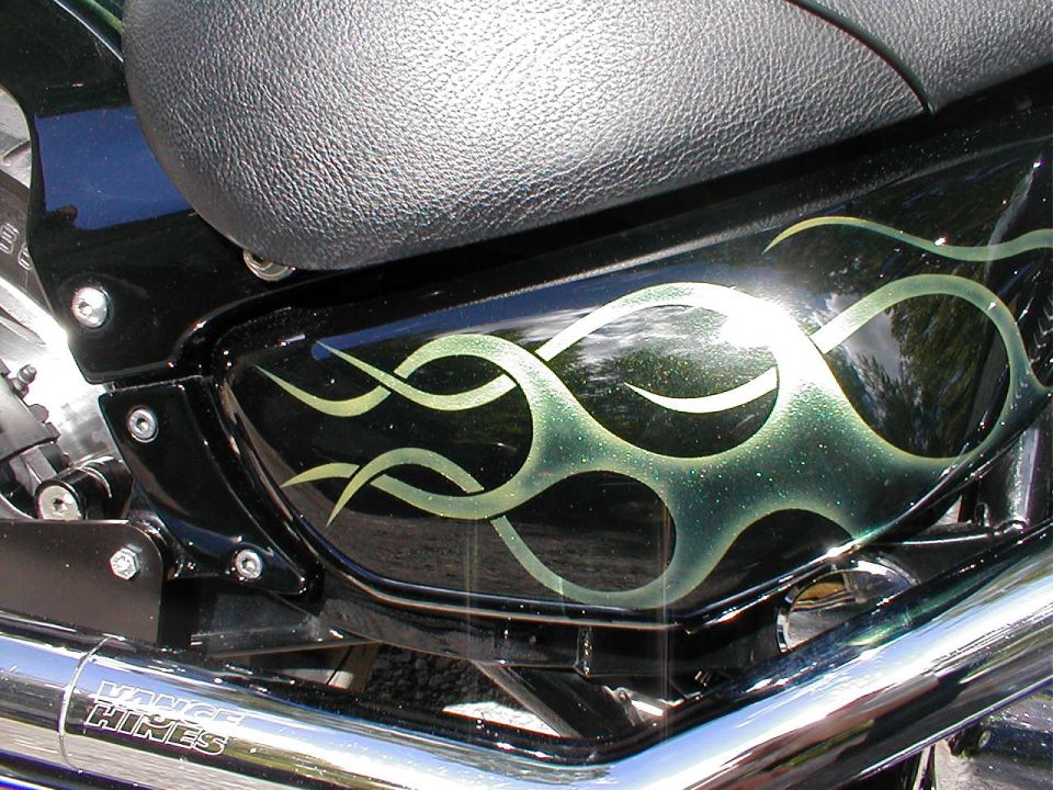 Green tribal flames on a black cruiser side cover above a Vance & Hines chrome muffler
