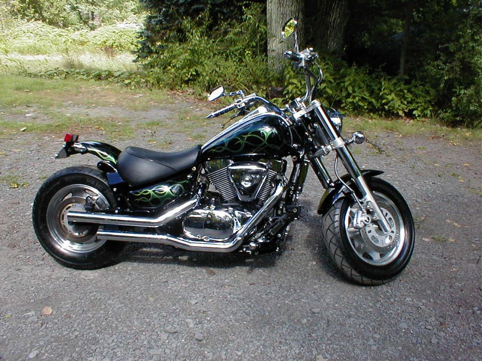Black V-twin cruiser motorcycle with green flame graphics and chrome exhaust on gravel