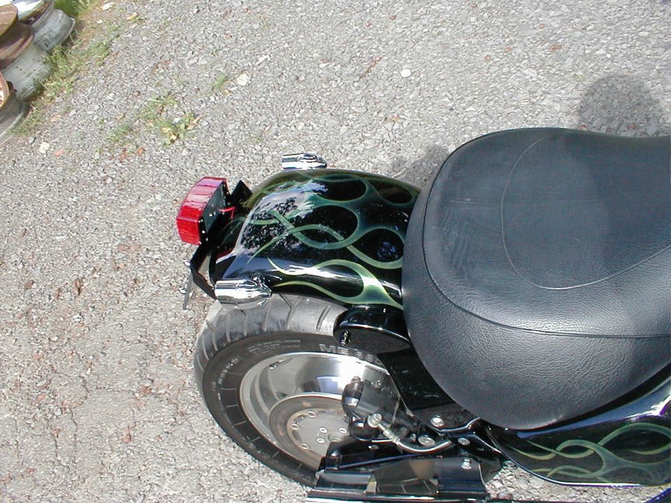 Motorcycle rear fender with green flames paint and black seat. Tire and taillight visible