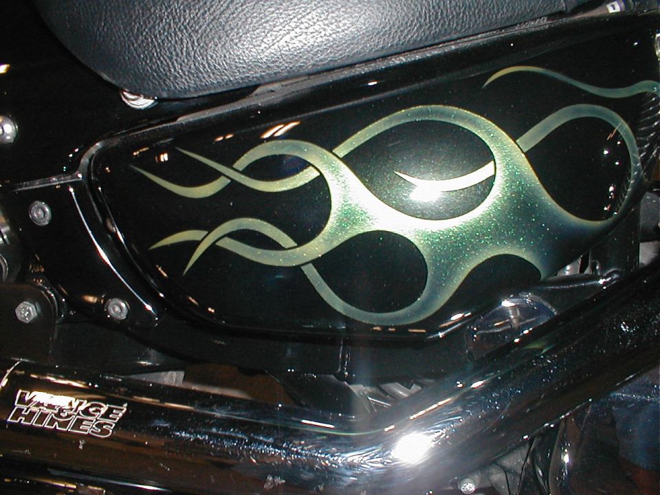 Close-up of a black motorcycle fuel tank with green and silver flame graphics. Vance & Hines exhaust pipe visible