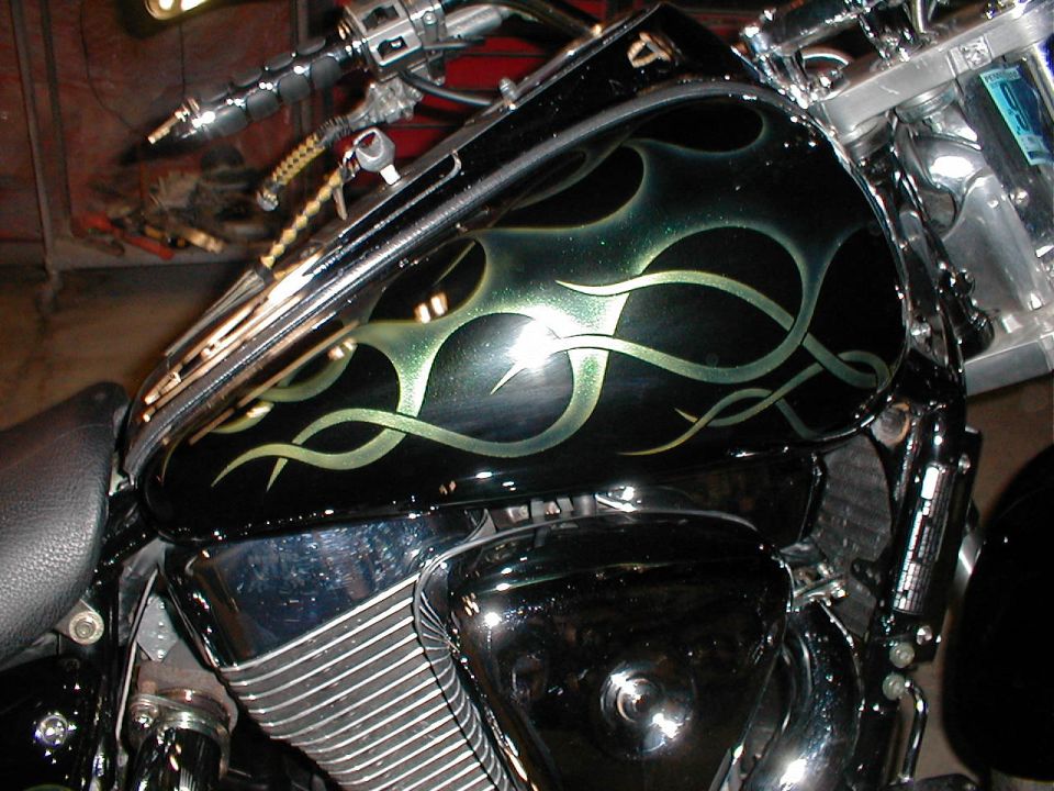 Motorcycle fuel tank with black and green flame paint job. Chrome engine parts visible