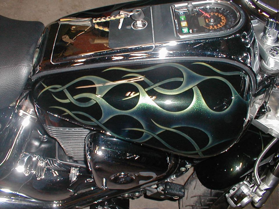 Motorcycle fuel tank with black and green flame paint, chrome accents, and a speedometer