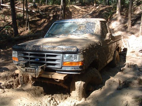 1993 Ford Bronco - This pickup truck is covered in mud while navigating a challenging off-road trail.