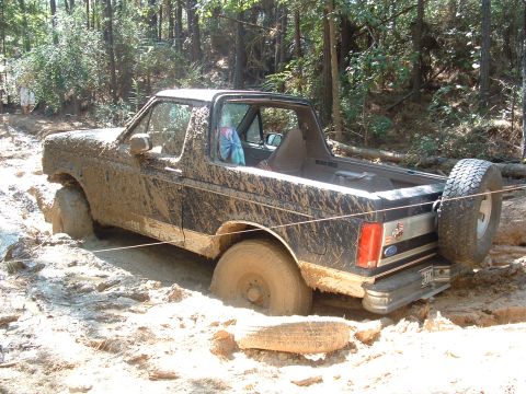 1993 Ford Bronco - A heavily mud-covered 1987 Ford Bronco is stuck off-road, with its tires deep in mud.