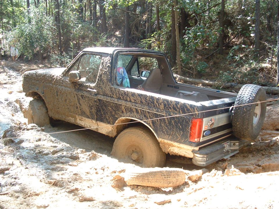 Topless Ford Bronco stuck axle-deep in a clay mud hole with a taut recovery line