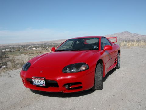 1999 Mitsubishi 3000GT - A red 1999 Mitsubishi 3000GT is parked outdoors with a scenic mountain landscape behind it.