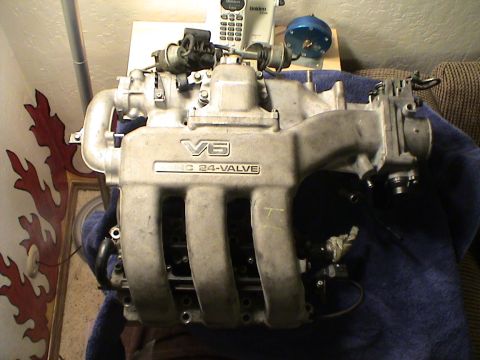1997 Ford Probe - A V6 24-valve engine intake manifold is displayed on a blue cloth, with a cordless phone and gauge visible behind it.