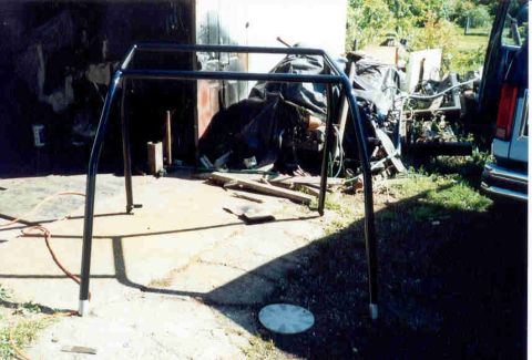 1989 Ford Bronco - A custom roll cage frame is set up outdoors near a garage and a blue vehicle.