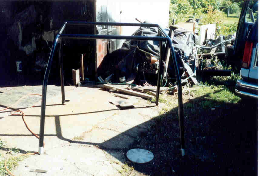 roll cage frame in front of a garage with a blue vehicle in the background