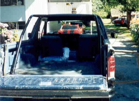 1989 Ford Bronco - Rear view of a 1989 Ford Bronco with its tailgate down, showing the interior and another car in the distance.
