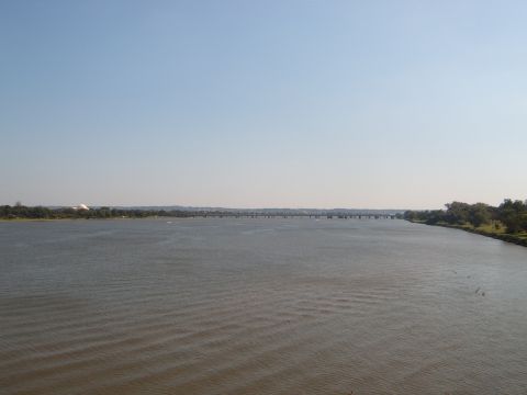1988 Ford Bronco - A wide river flows under a clear sky with a long bridge spanning the water in the distance.