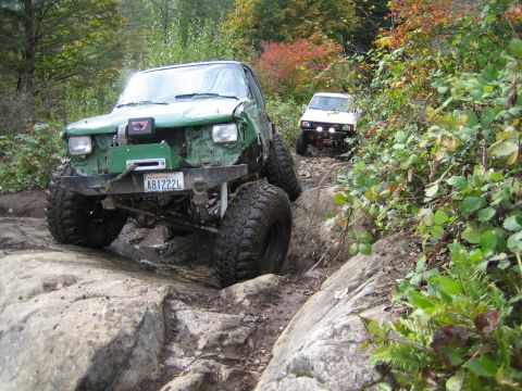 1990 Ford Bronco - Two modified off-road vehicles navigate a challenging rocky trail during autumn.