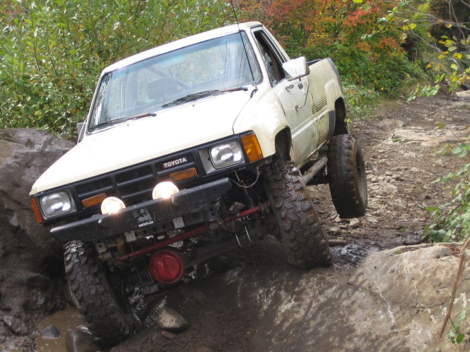 White Toyota pickup truck with lifted suspension navigating rocky terrain