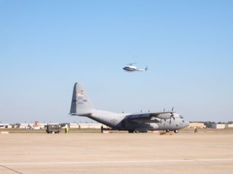 1988 Ford Bronco - A large military transport aircraft is parked on an airfield, with a helicopter flying overhead.