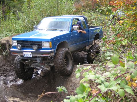 1990 Ford Bronco - A blue pickup truck tackles a challenging muddy trail with its large off-road tires.