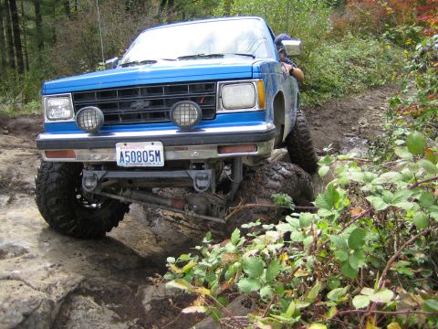 1990 Ford Bronco - A blue pickup truck with off-road modifications is shown traversing a challenging rocky path.